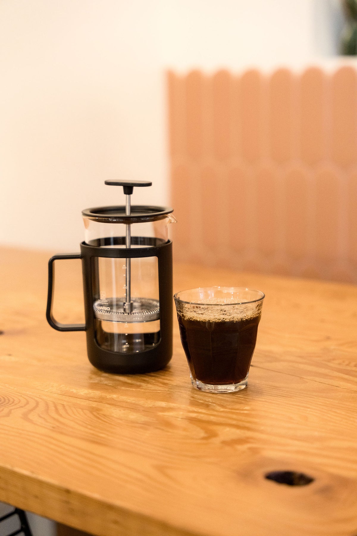 Hario French press beside a glass of brewed coffee on a café table