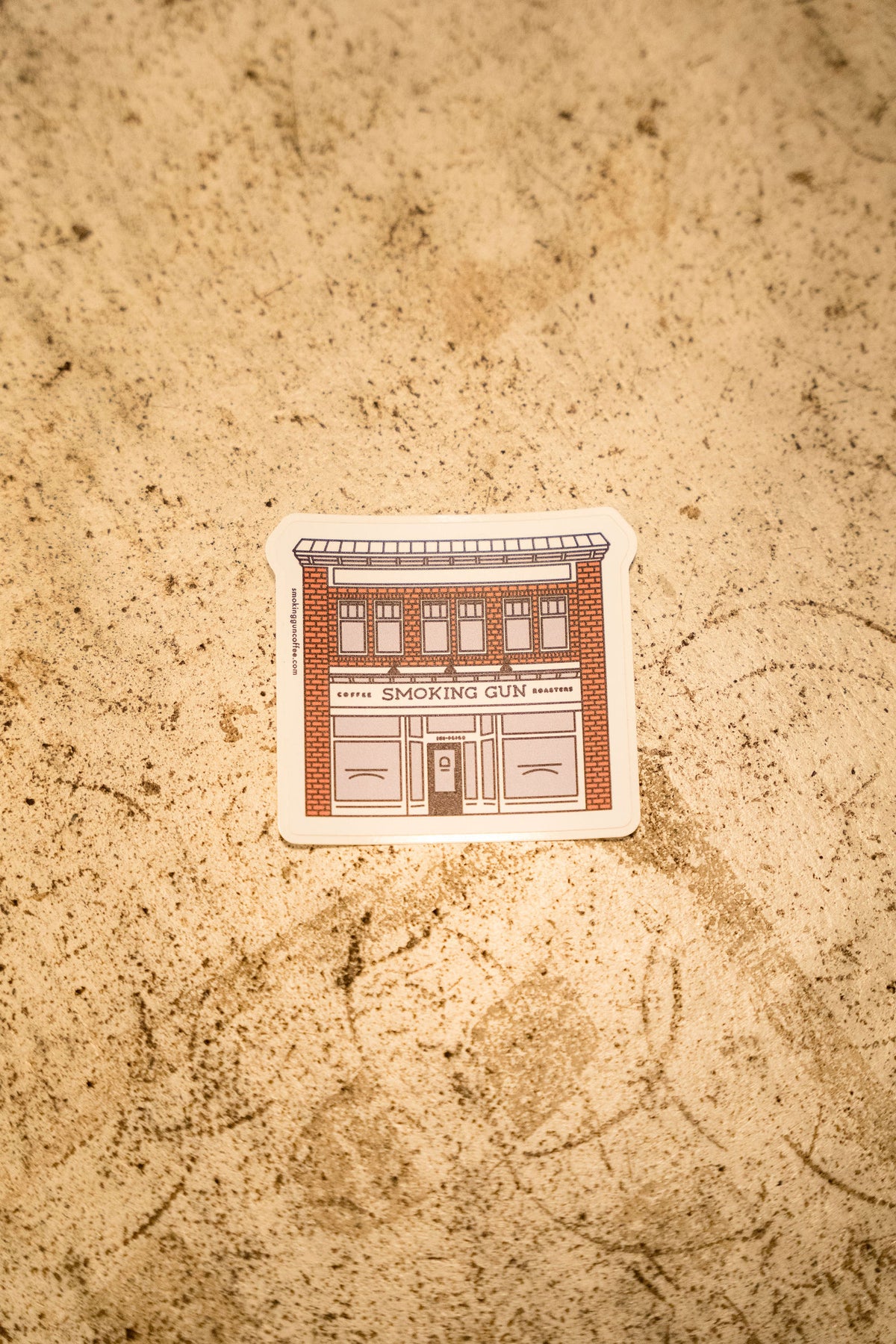 Smoking Gun Café die-cut sticker on a stone counter